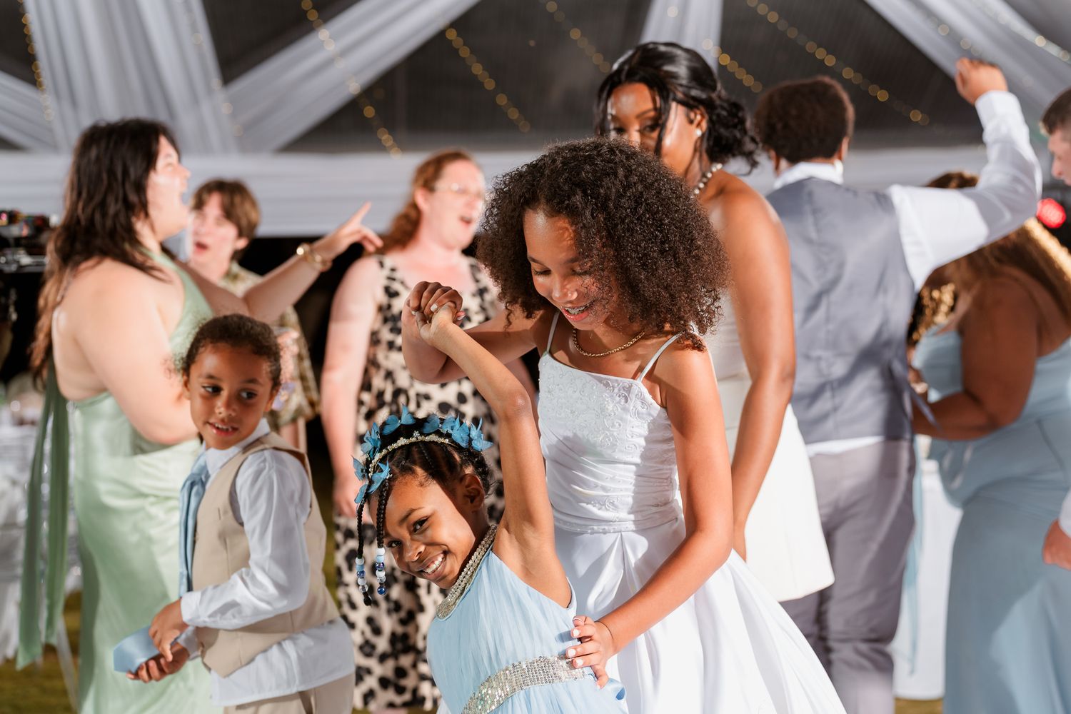 Joyful wedding reception dancing with guests in elegant attire under a white tent.