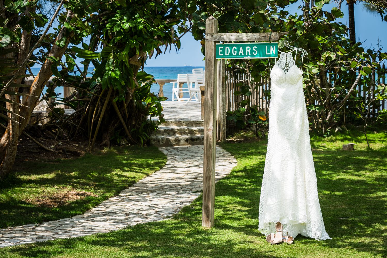 White wedding dress hanging on a street sign at Edgar's Lane, with a tropical beach pathway and lush greenery in the background.
