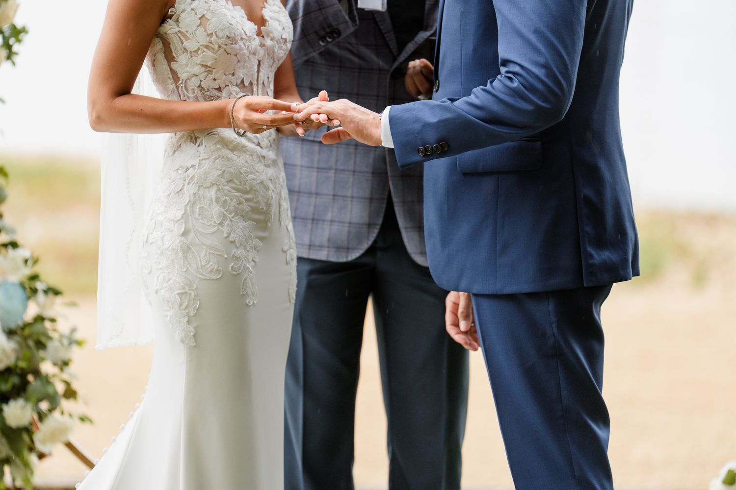 Close up of couple exchanging wedding rings during outdoor ceremony with officiant looking on.