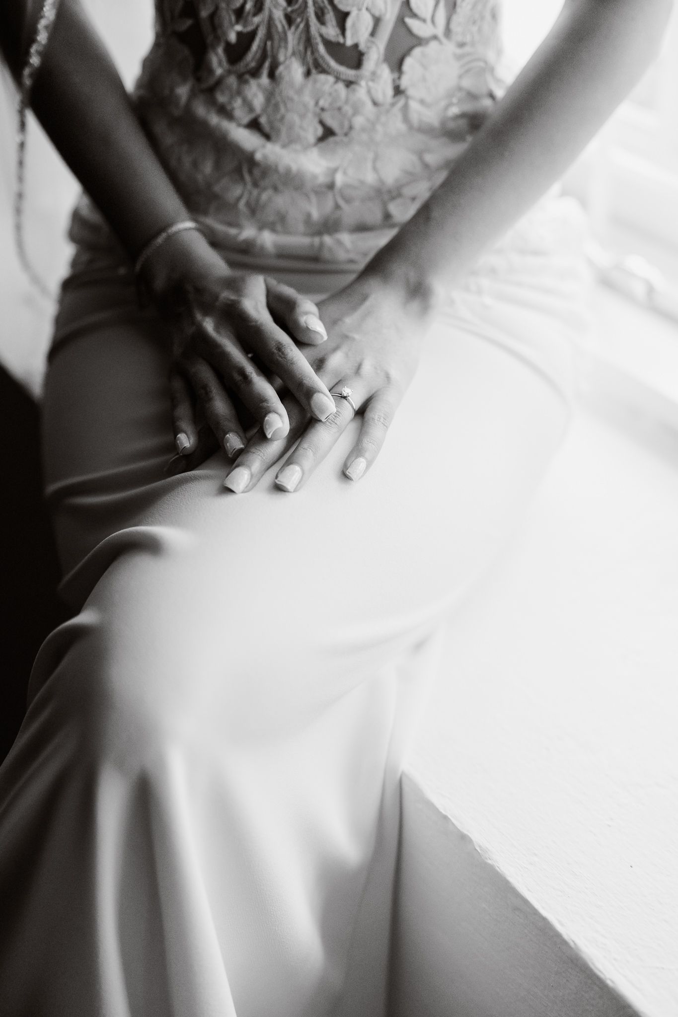 Detailed black and white closeup shots of a bride's hands resting on her white wedding dress.
