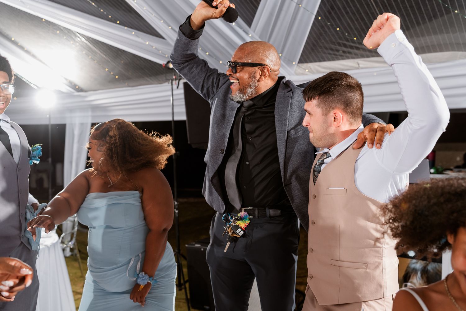 Diverse group of people dancing joyfully at an outdoor wedding reception celebration at night.