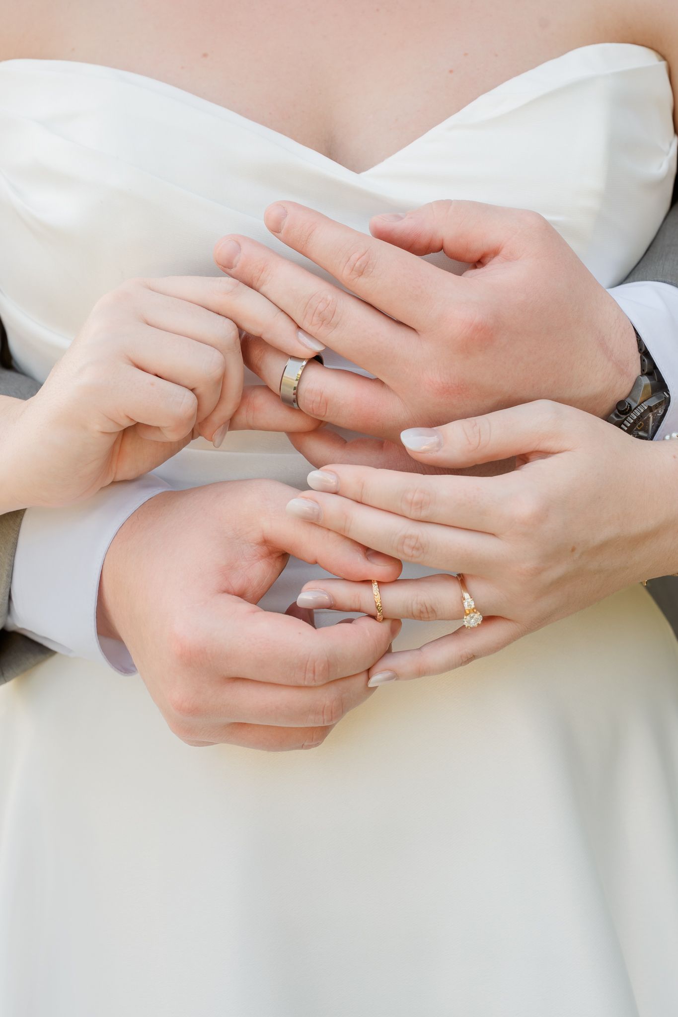 Newlywed couple holding hands together showing wedding rings, bride in white dress and groom in suit.