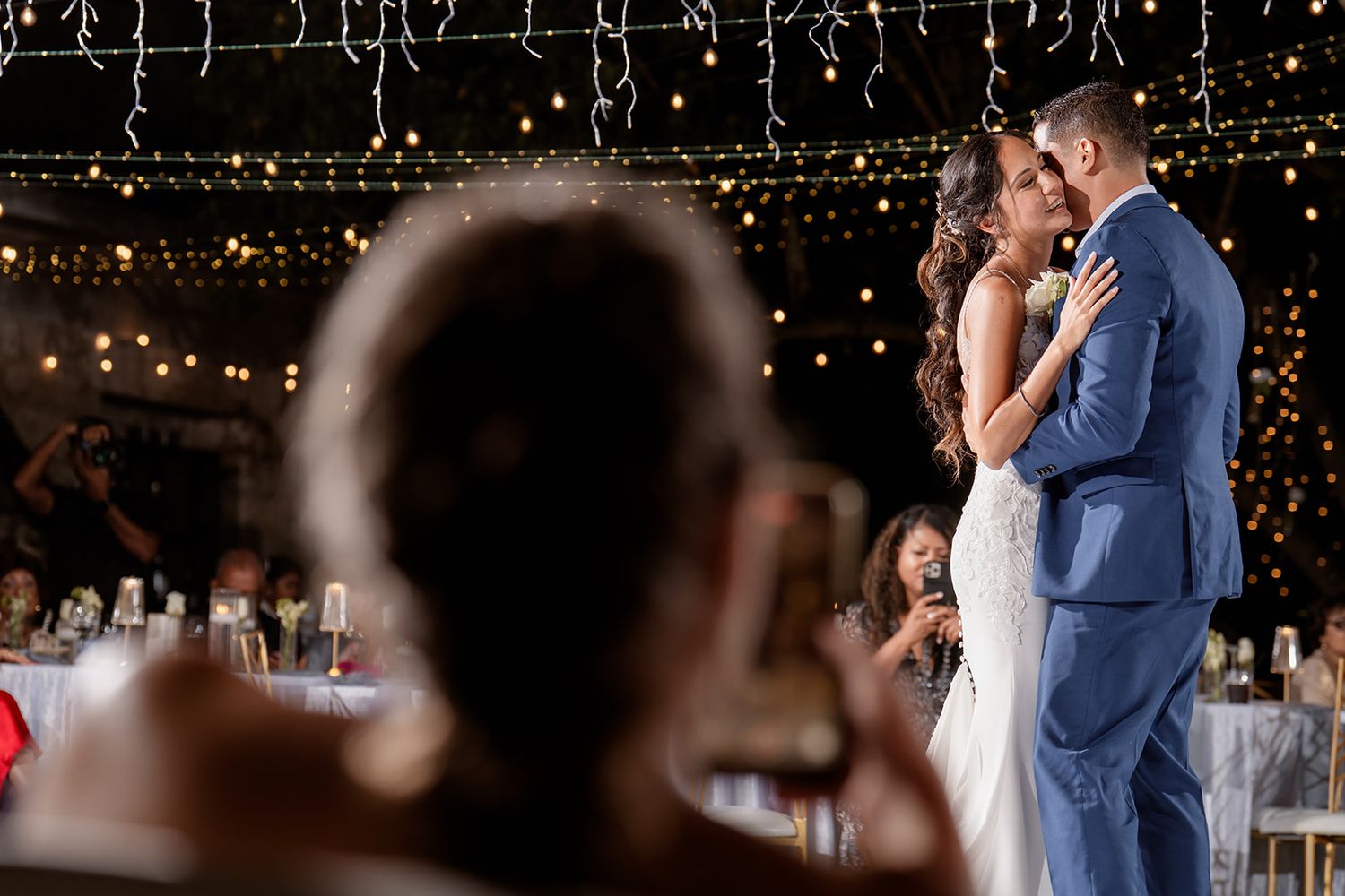 A couple shares their first dance as newlyweds under twinkling lights at an elegant evening wedding reception.