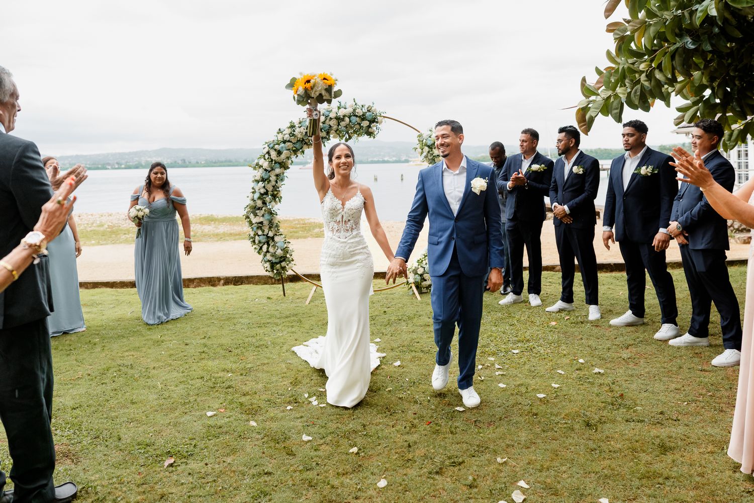 A joyful married couple walks down the aisle at their outdoor beach wedding ceremony with guests cheering.
