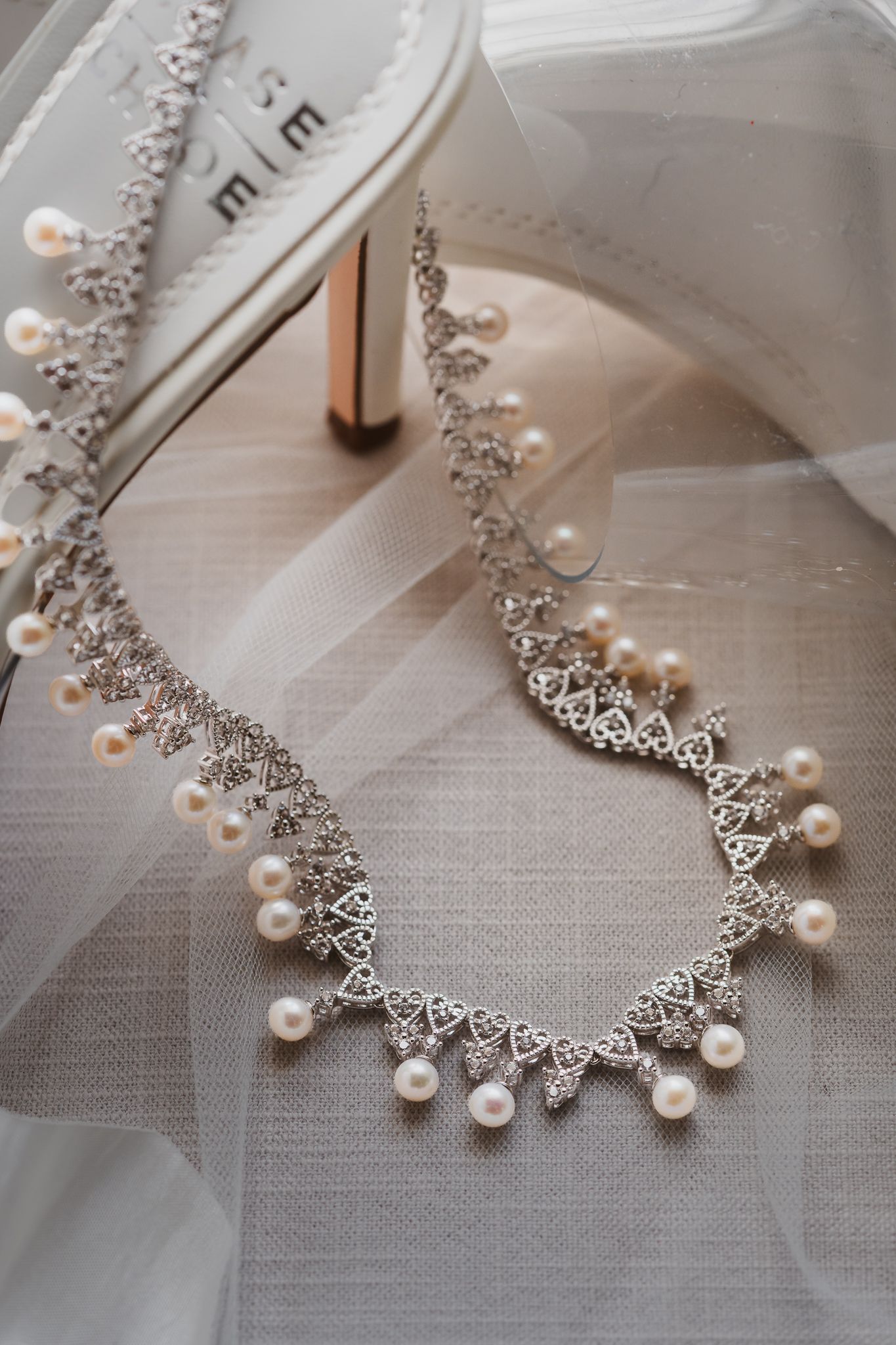Elegant pearl and silver Celtic knot bridal necklace draped on white veil beside ivory wedding heels.