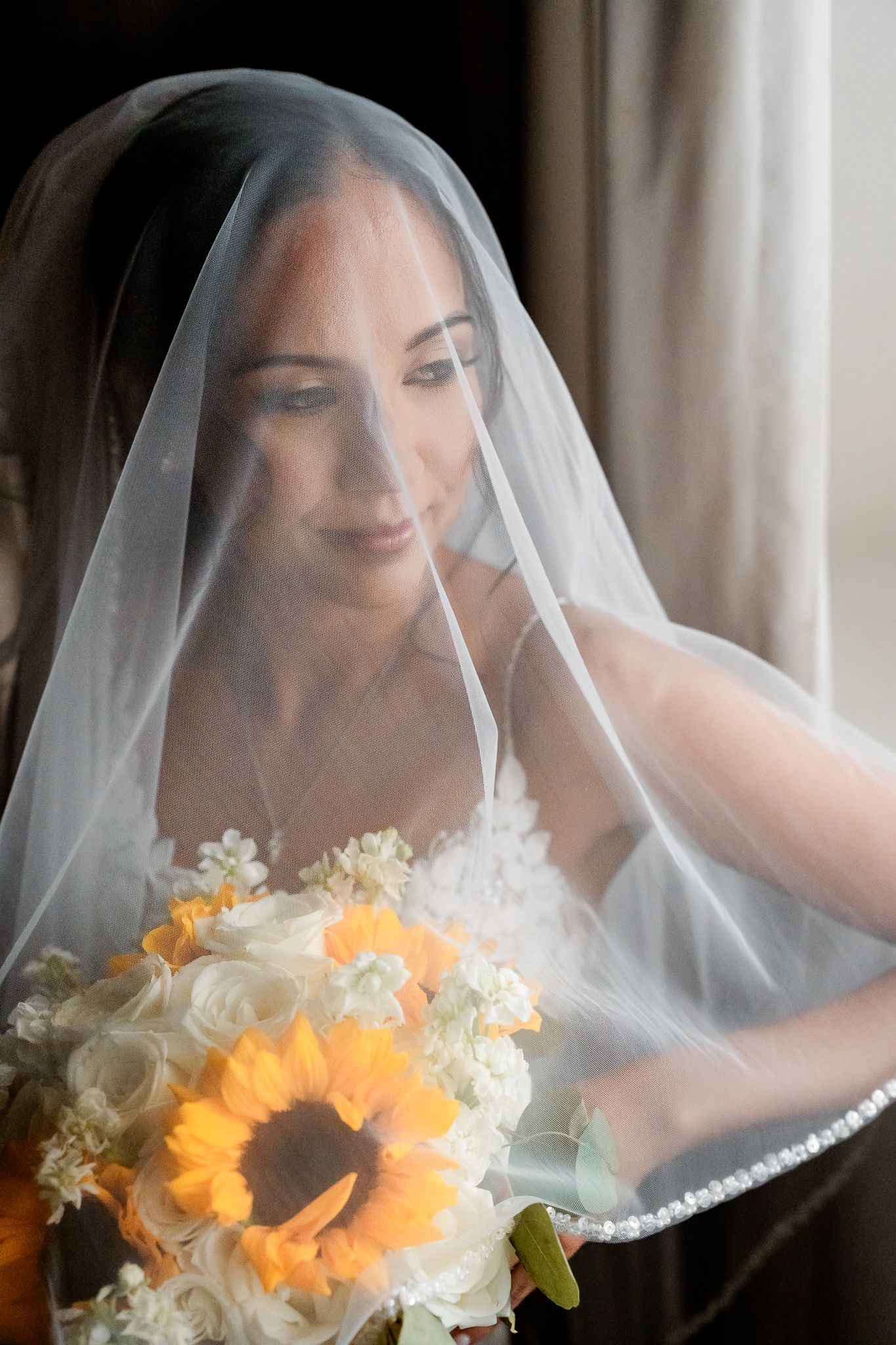 A bride in white veil poses with vibrant sunflowers and white flowers creating a romantic bridal portrait series.