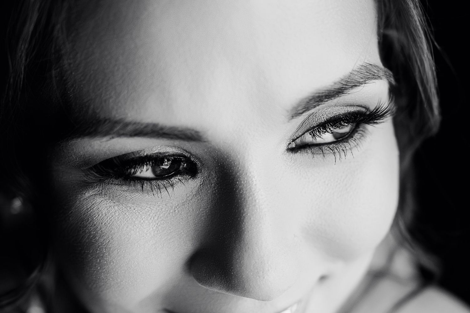 Monochromatic macro shot focusing on expressive eye and lashes with dramatic lighting.