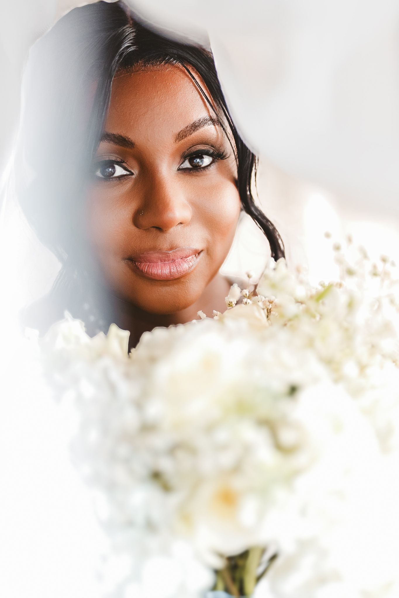 Beautiful Black bride holding white floral bouquet, wearing veil, with elegant makeup on her wedding day.