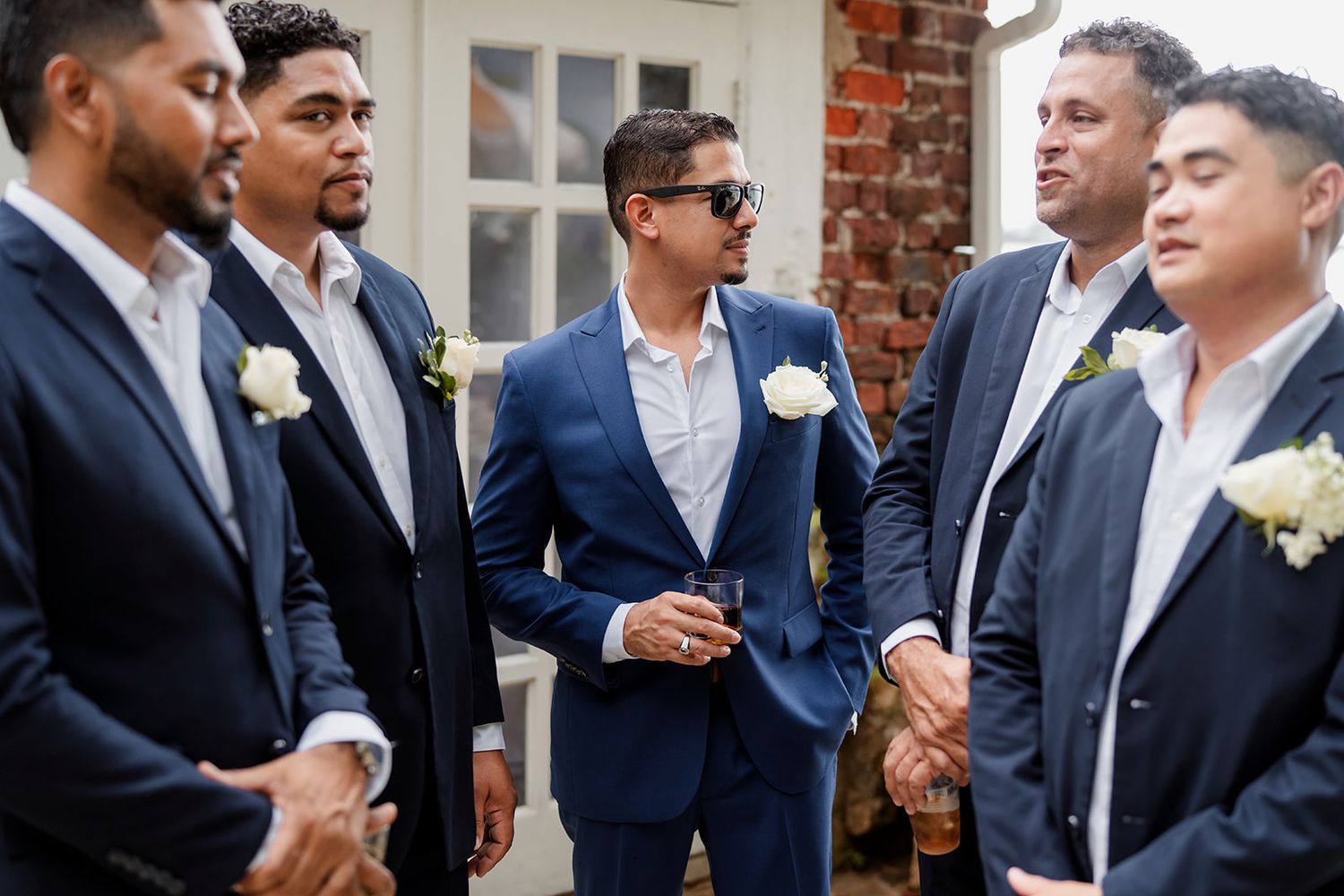 A group of people in navy suits stand in conversation at a formal event outdoors.