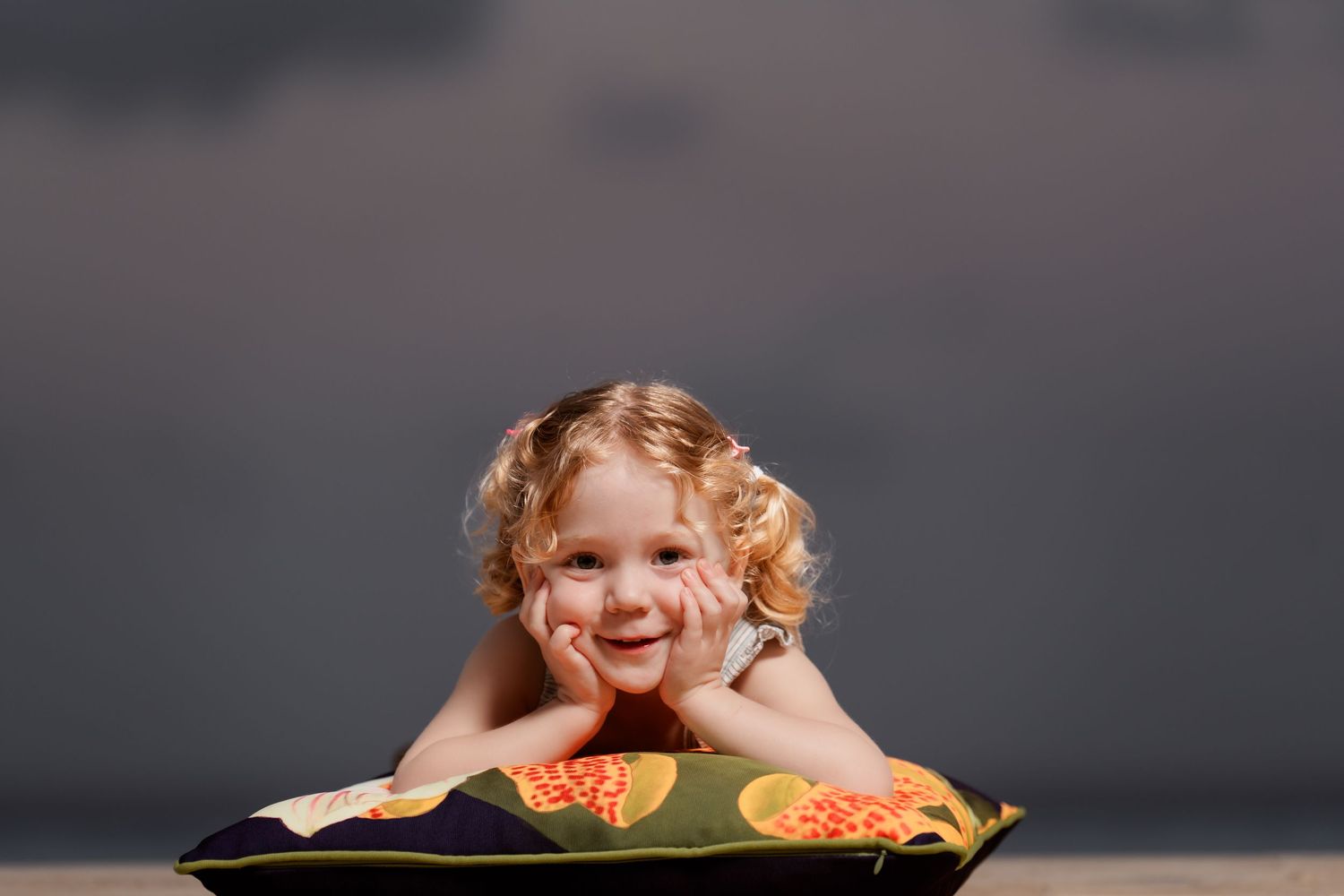 Happy child with curly hair leaning over a tray of cookies against a dark grey background.