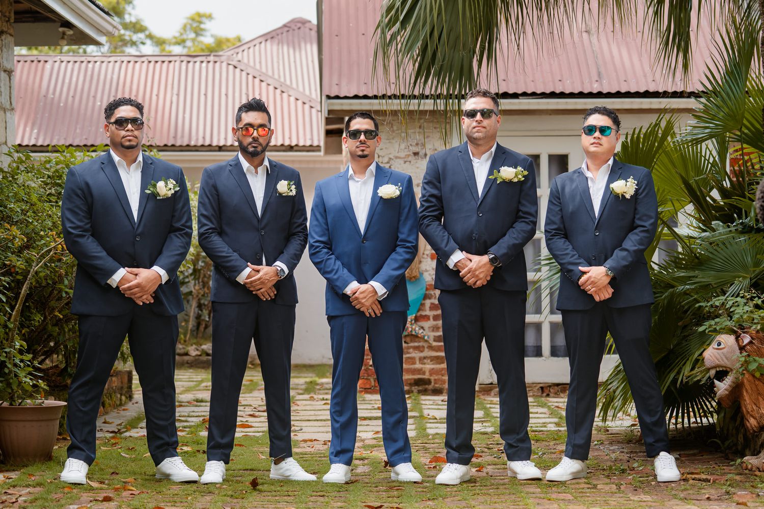 Groomsmen in coordinating blue suits and white sneakers posing outdoors with palm trees.