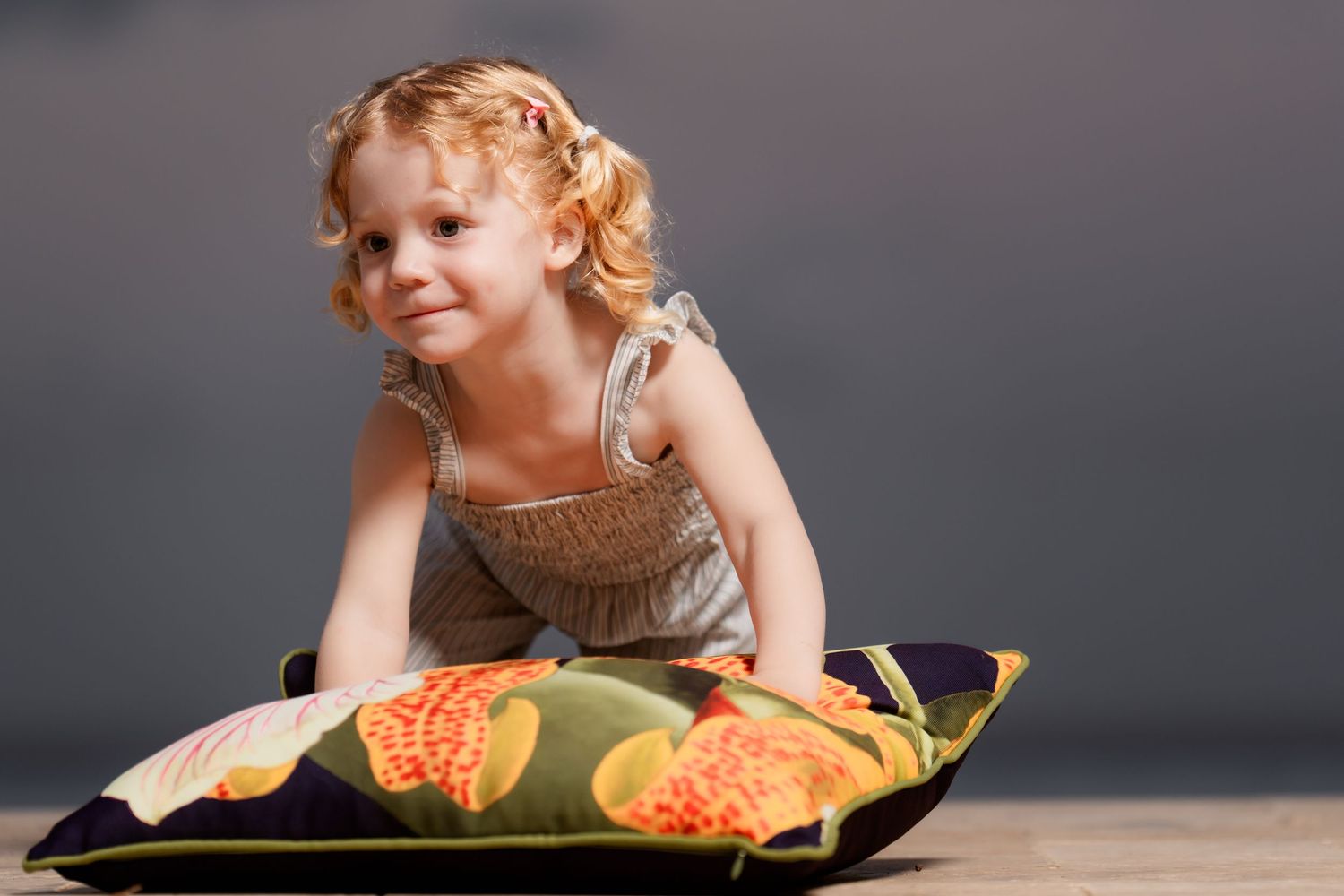 Small child in overalls laying on a decorative pillow against a dark studio backdrop.