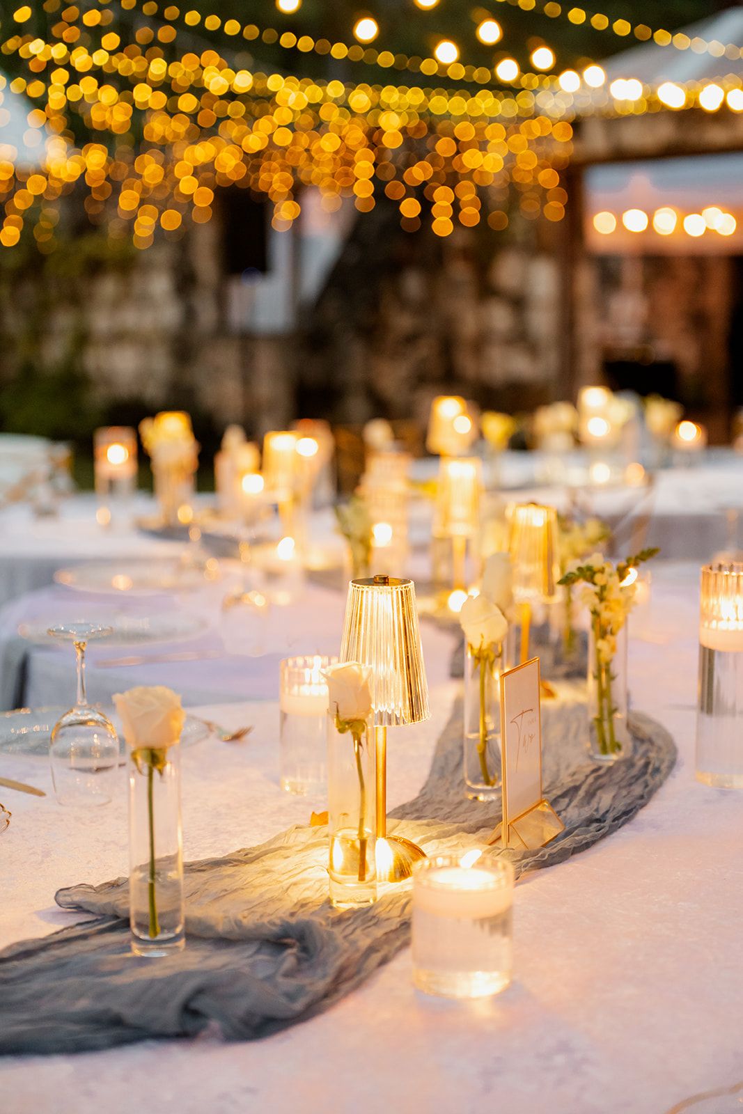 An elegant outdoor reception table with glowing candles and string lights creating a romantic ambiance.