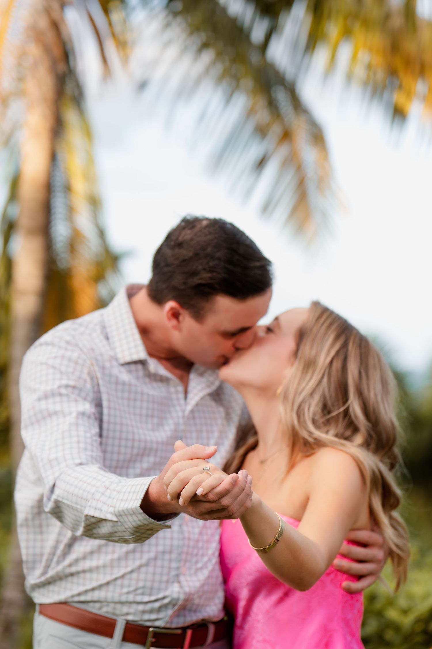 Romantic couple shares a tender kiss while dancing beneath palm trees in a tropical setting.