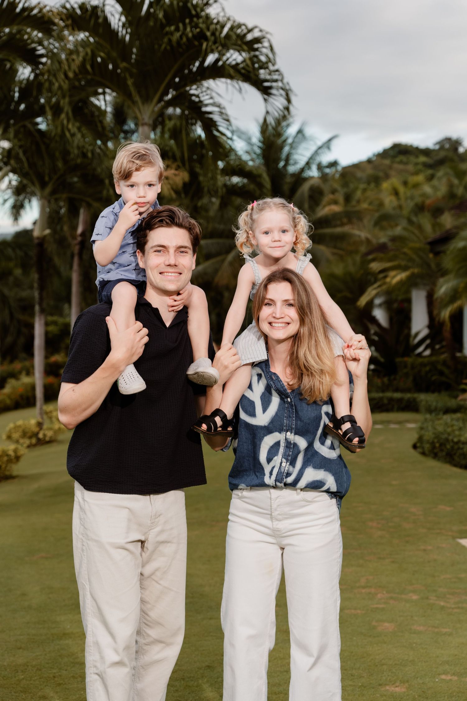 Cheerful family in coordinated casual outfits posing together outdoors with palm trees in the background.
