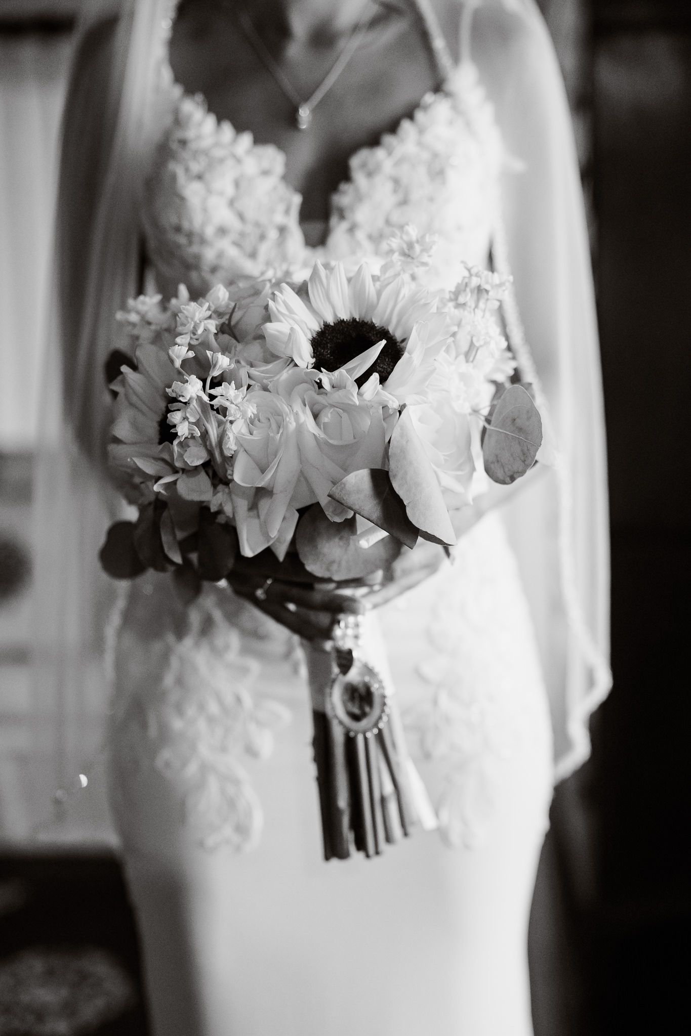 Black and white close-up of a bride in lace wedding dress holding an elegant bouquet with sunflowers and roses.