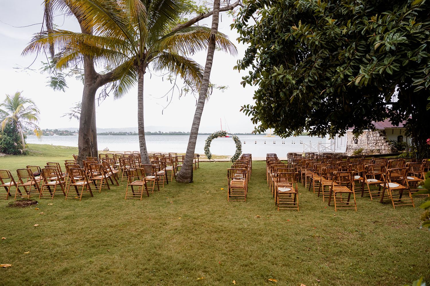 Rows of wooden chairs set up on a grassy beachfront lawn with palm trees and ocean views for an outdoor ceremony.