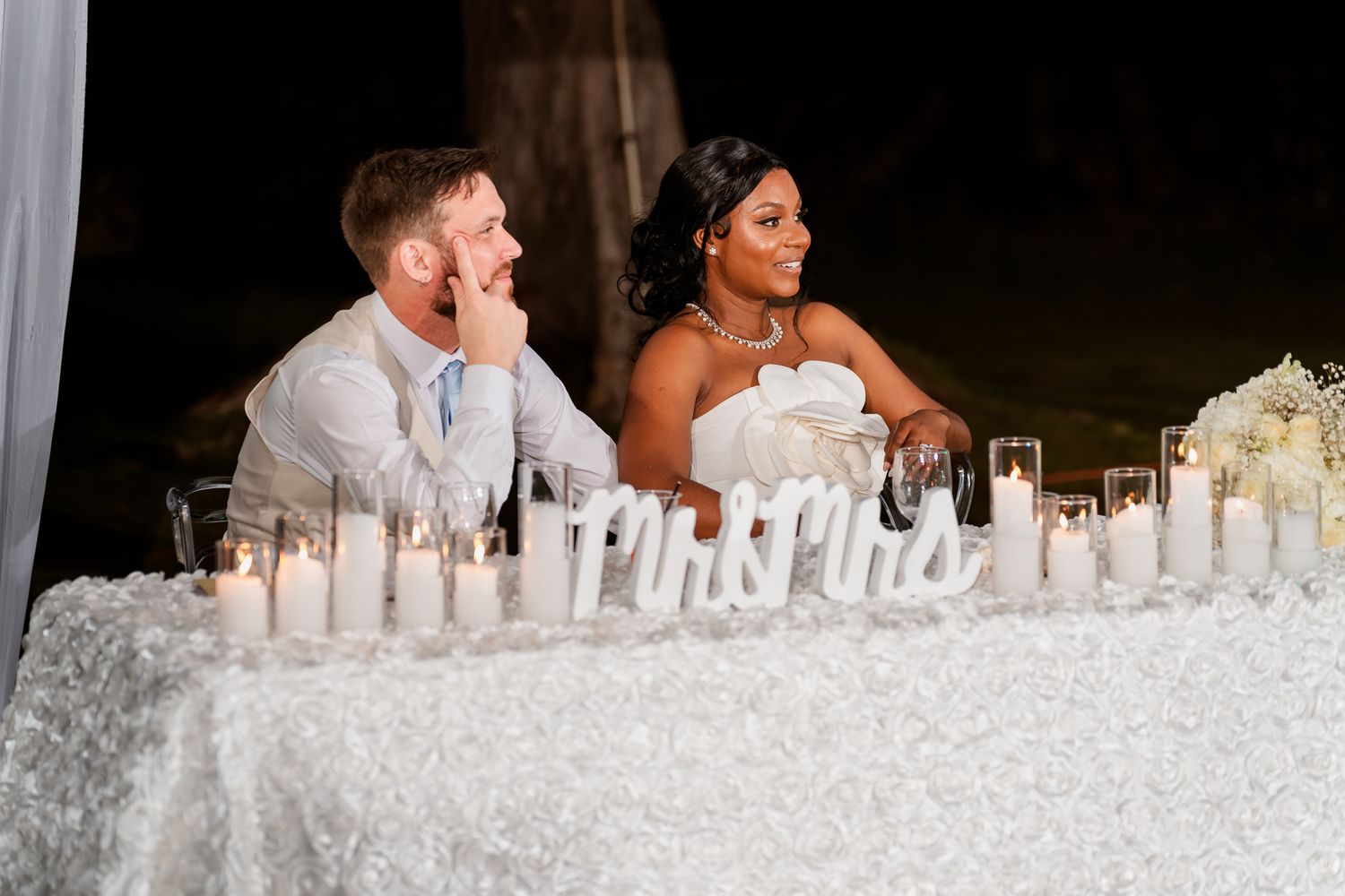 Interracial couple seated at a decorated wedding sweetheart table with candles and Mr. & Mrs. signs.
