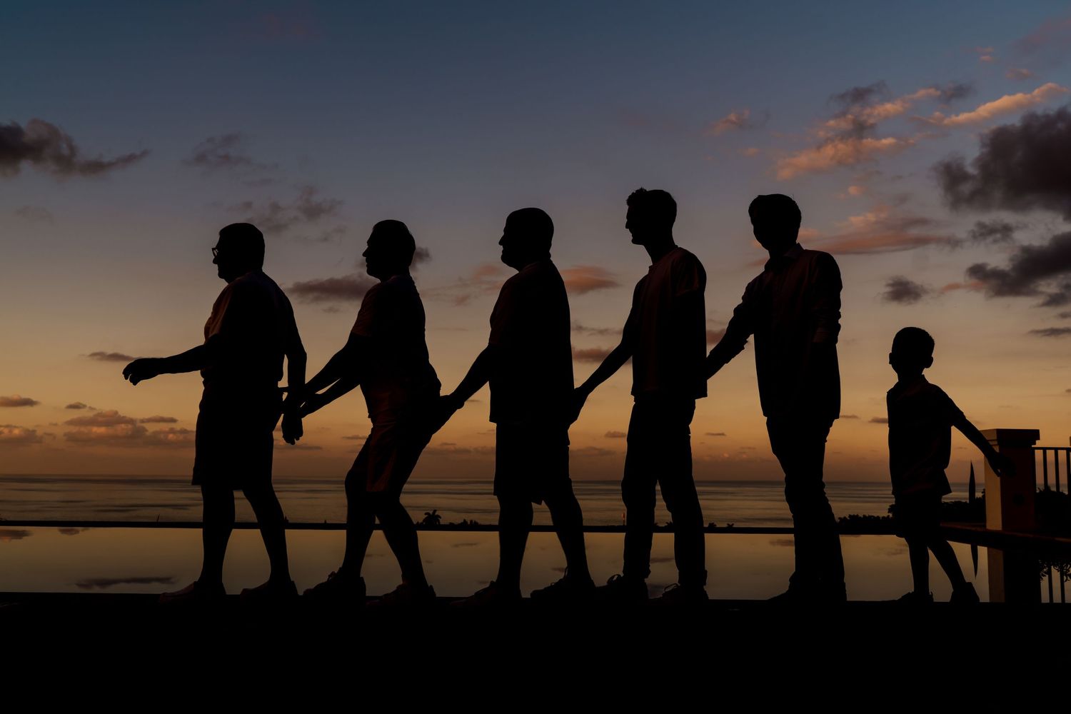 Silhouettes of six people walking in a line along the beach at sunset against an orange and purple sky.