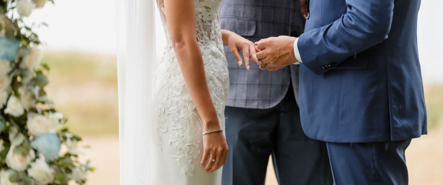 Close-up view of a couple at a wedding ceremony, with focus on formal attire and clasped hands.