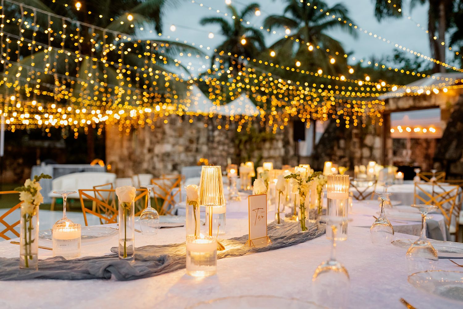 Elegant outdoor wedding reception setup with glowing candle centerpieces and string lights creating a romantic ambiance.