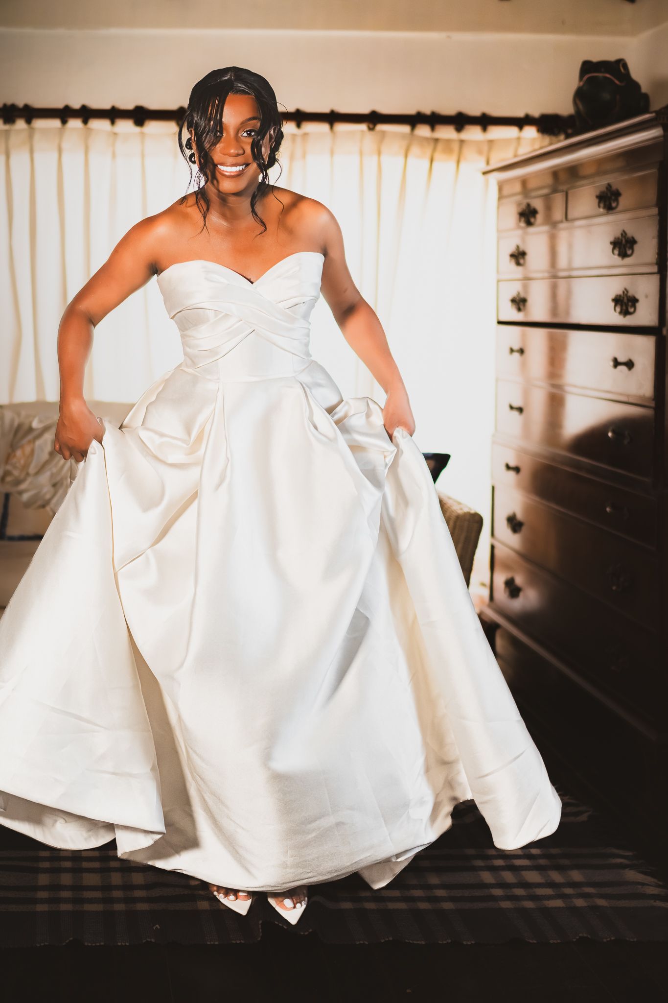 Joyful Black bride in strapless white ballgown wedding dress twirling in a sunlit bedroom.