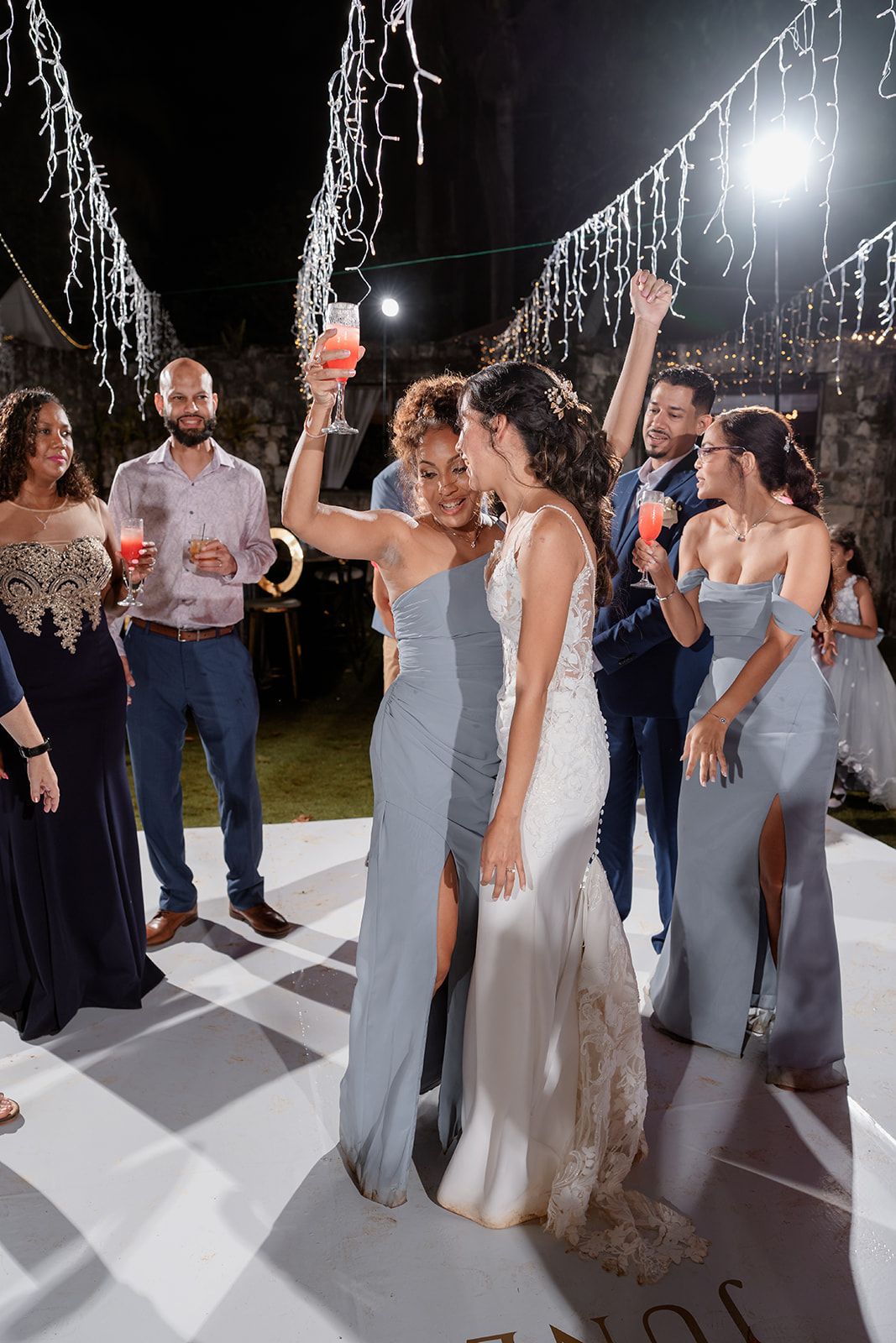 Wedding guests dance and celebrate under glowing icicle lights at an outdoor evening reception.