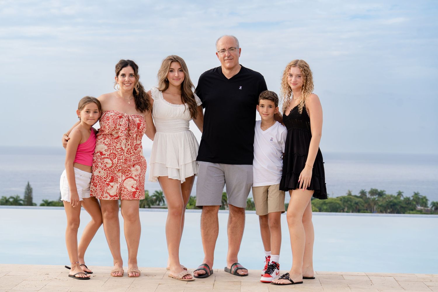 A group of people pose together on a beach at sunset with calm water and distant shore in the background.