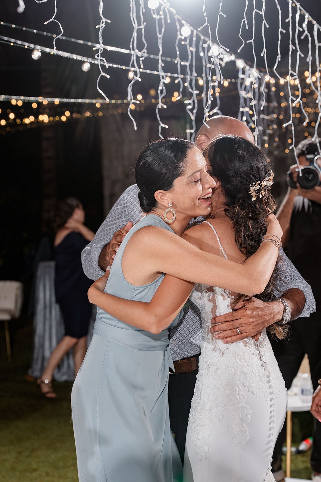 Emotional wedding scene under twinkling lights showing heartfelt embrace between two people during reception celebration.