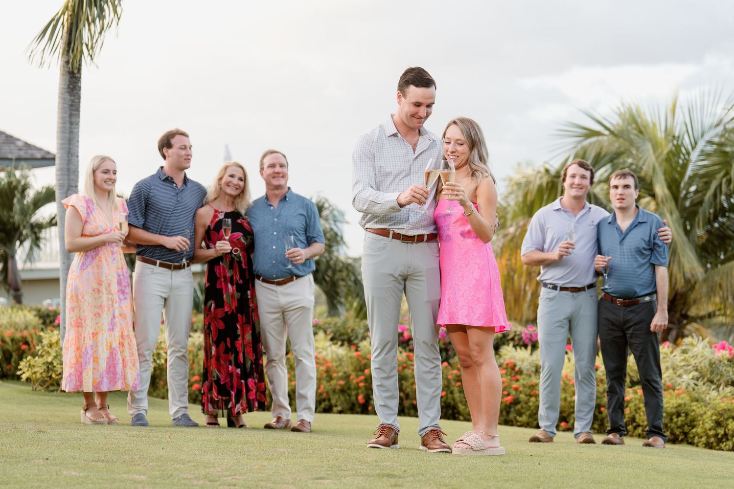 A group gathers for a celebratory moment on a lush green lawn with palm trees and tropical landscaping in the background.