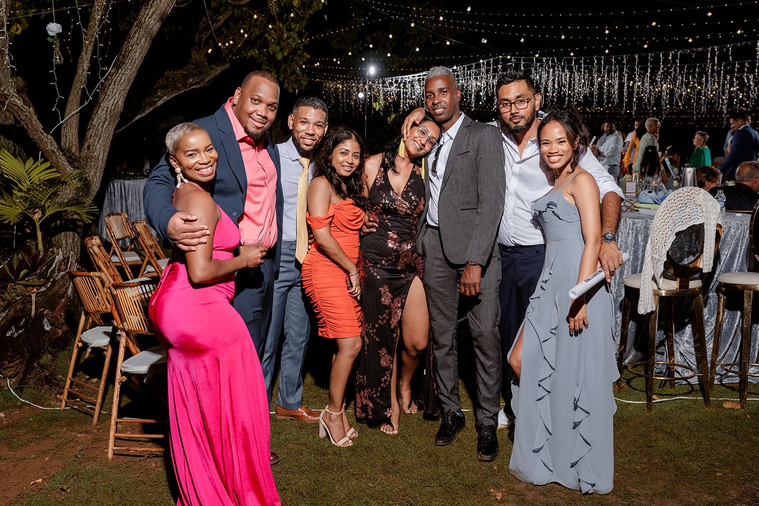 People dancing and socializing at an outdoor party or celebration with string lights overhead.
