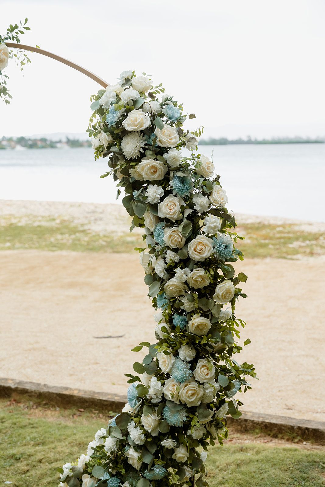 Elegant white floral arrangements with roses and eucalyptus create a romantic beach wedding ceremony backdrop.