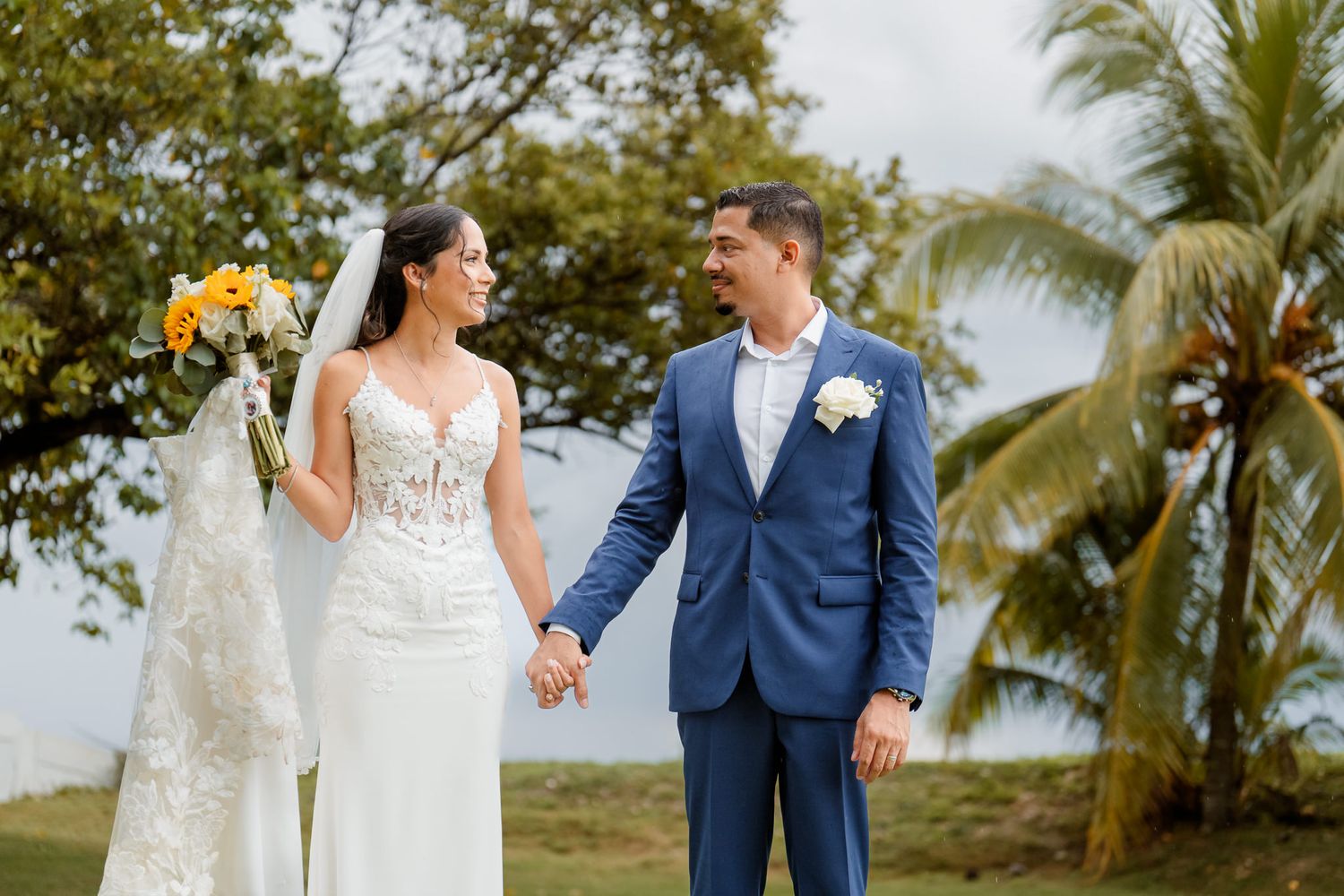 A bride and groom share intimate moments in a tropical setting with palm trees and greenery in the background.