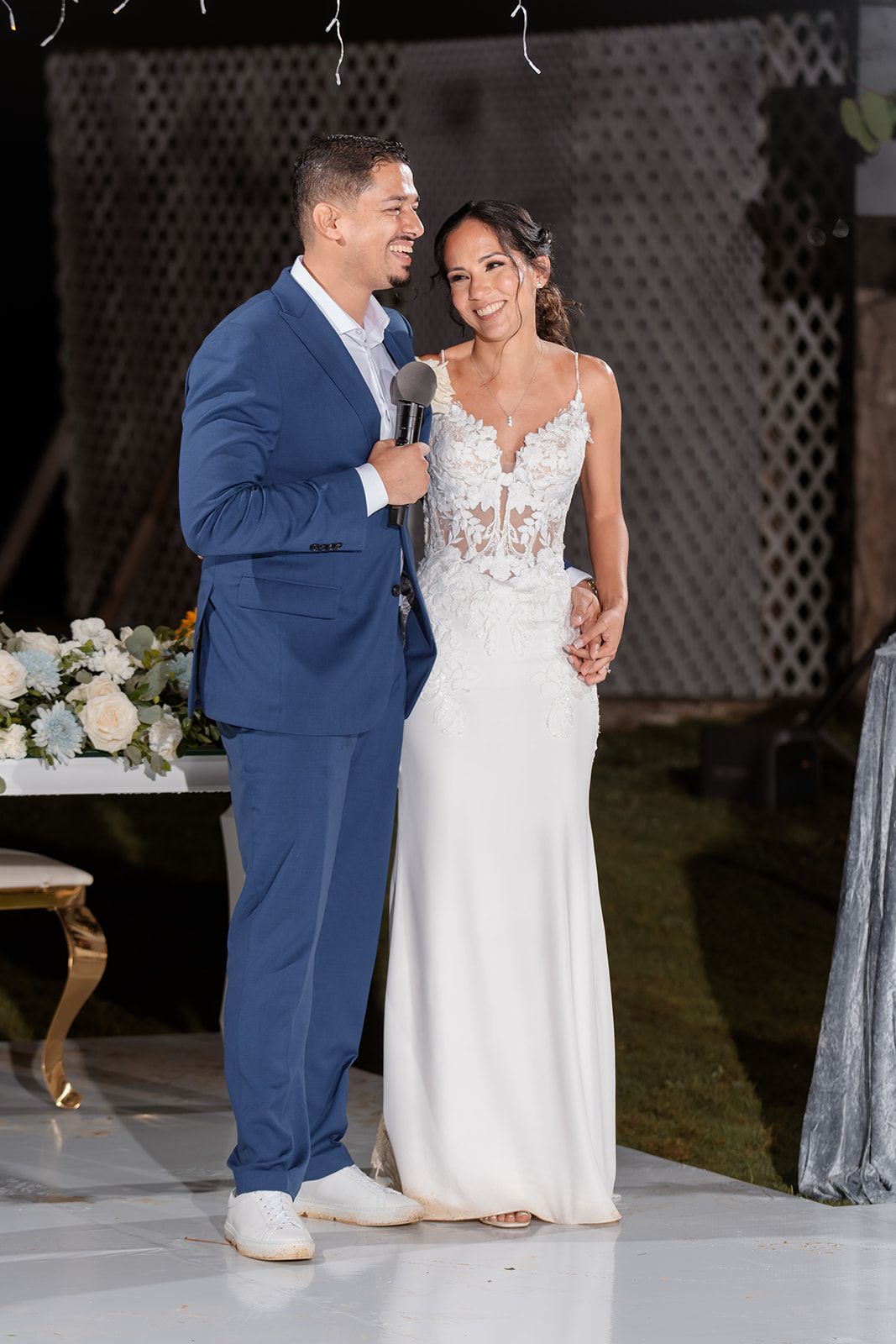 The bride in a white lace gown dances with the groom wearing a navy blue suit during a romantic first dance.