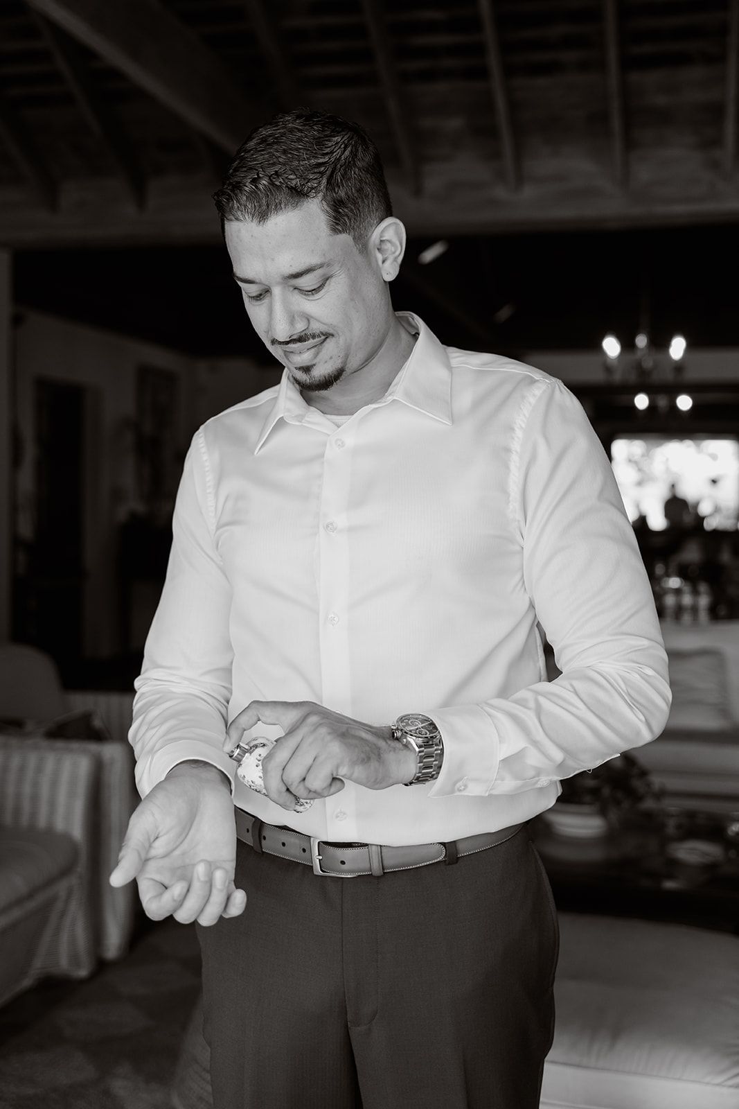A person in a white dress shirt and dark pants checks their watch in a dim indoor setting at an event.