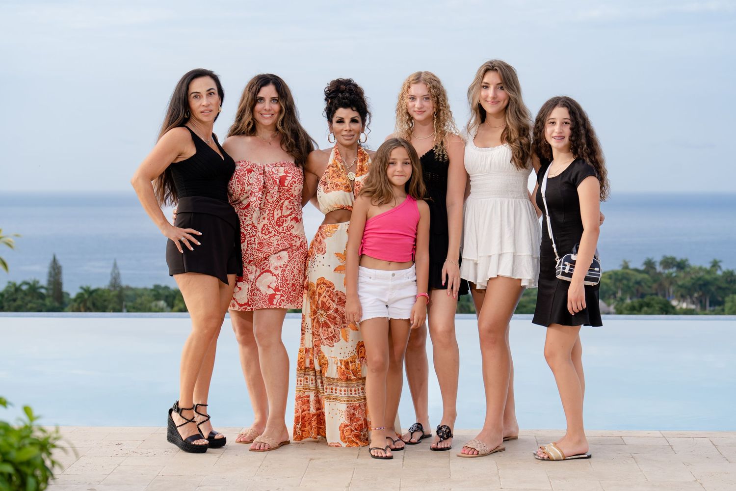 A group of people pose together for a photo by an infinity pool overlooking the ocean at a tropical resort.