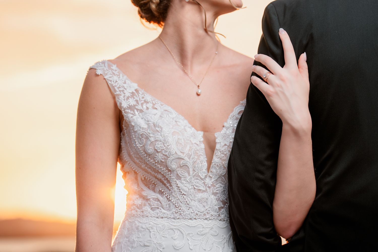 Close-up of elegant lace wedding dress detail against sunset with delicate necklace.