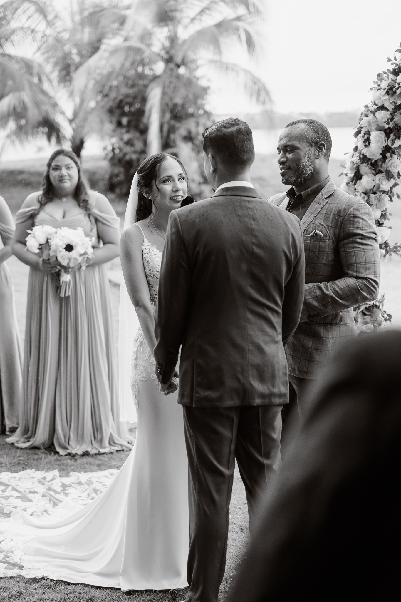 Black and white wedding ceremony on a tropical beach with palm trees and bridesmaids in flowing gowns.