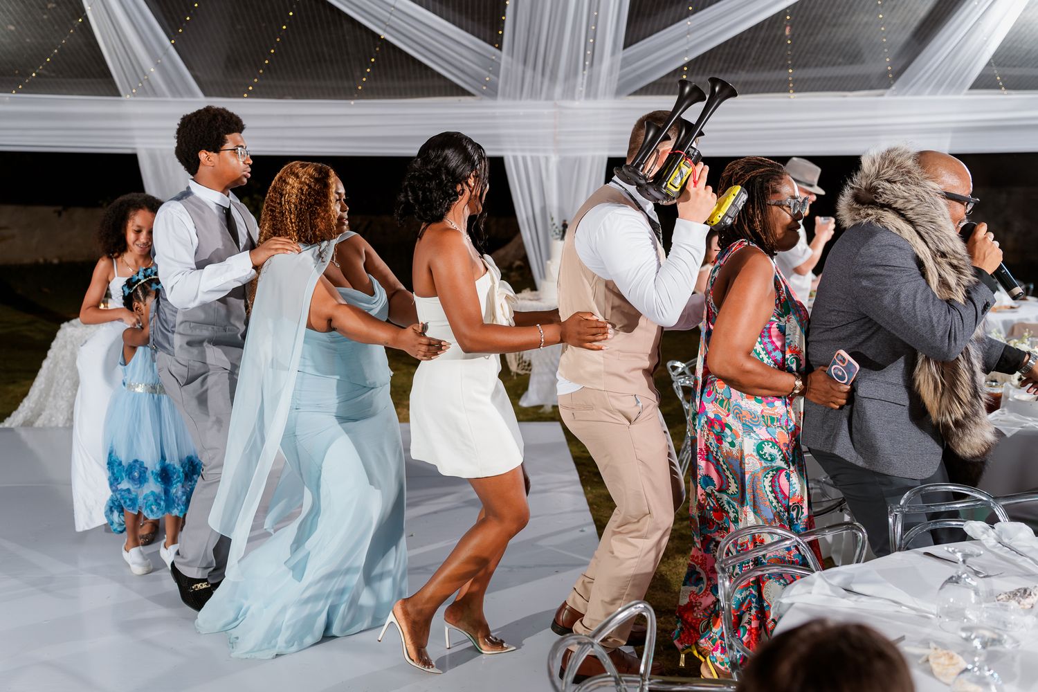 Guests dancing joyfully at an elegant outdoor wedding reception under a white draped tent.