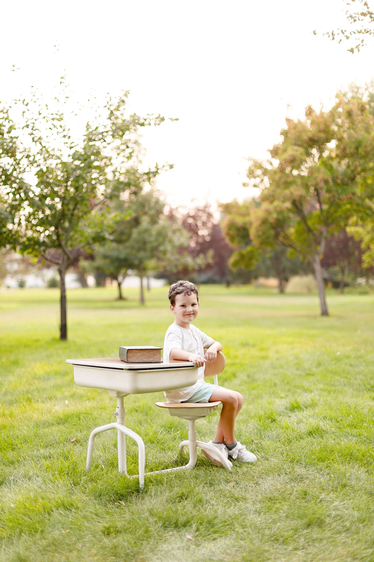 Child sitting at vintage school desk in sunny outdoor park setting.