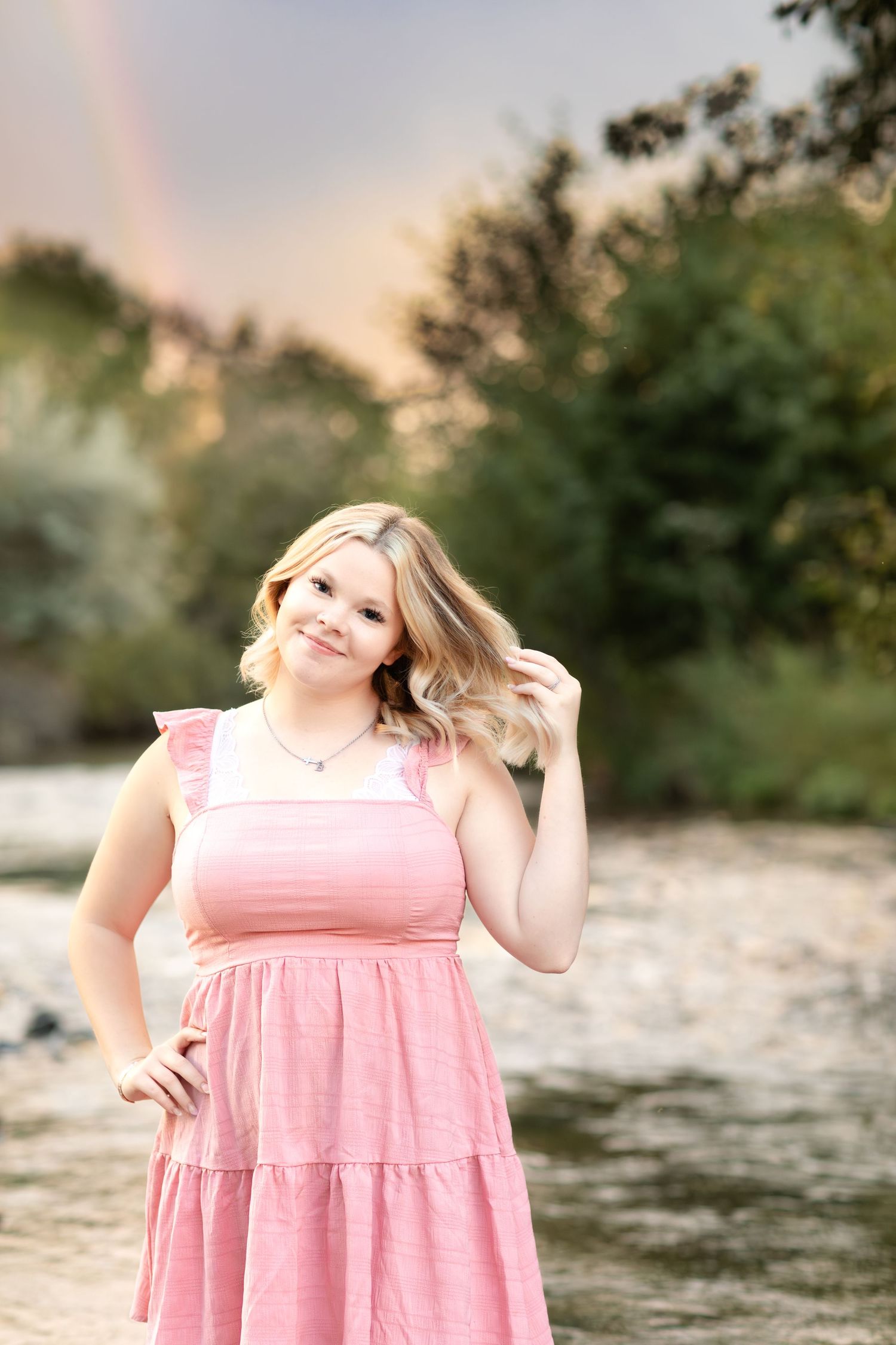 Sunlit outdoor portrait in pink dress against natural backdrop with rocks and trees.