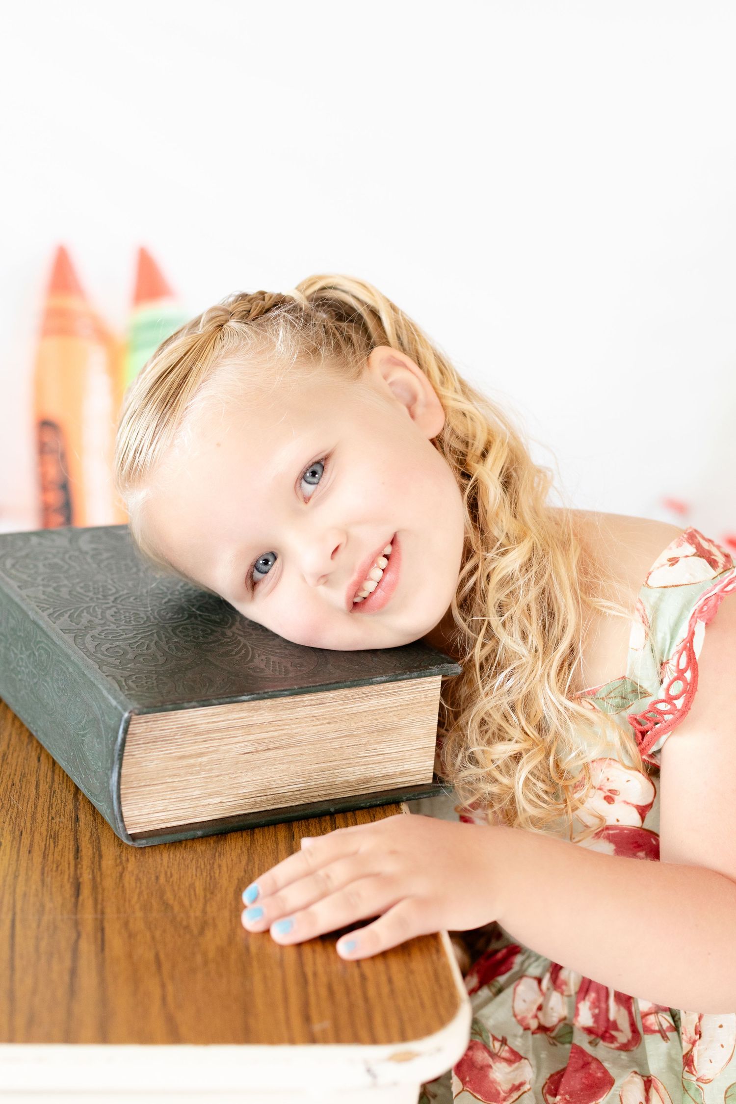 A child rests their head on a thick book while laying on a wooden surface in a series of similar poses.