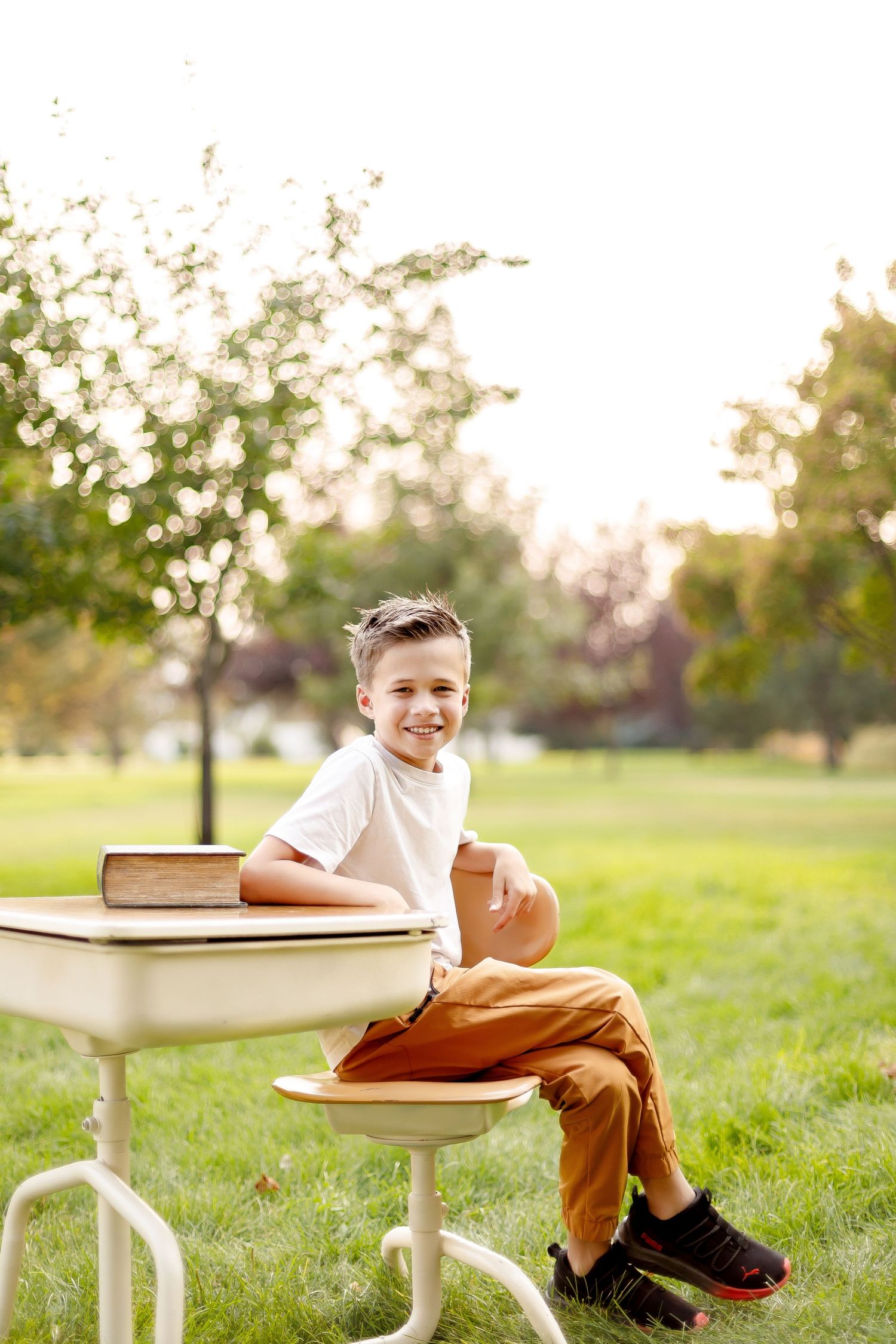 A vintage white school desk sits on green grass in a sunny park setting.