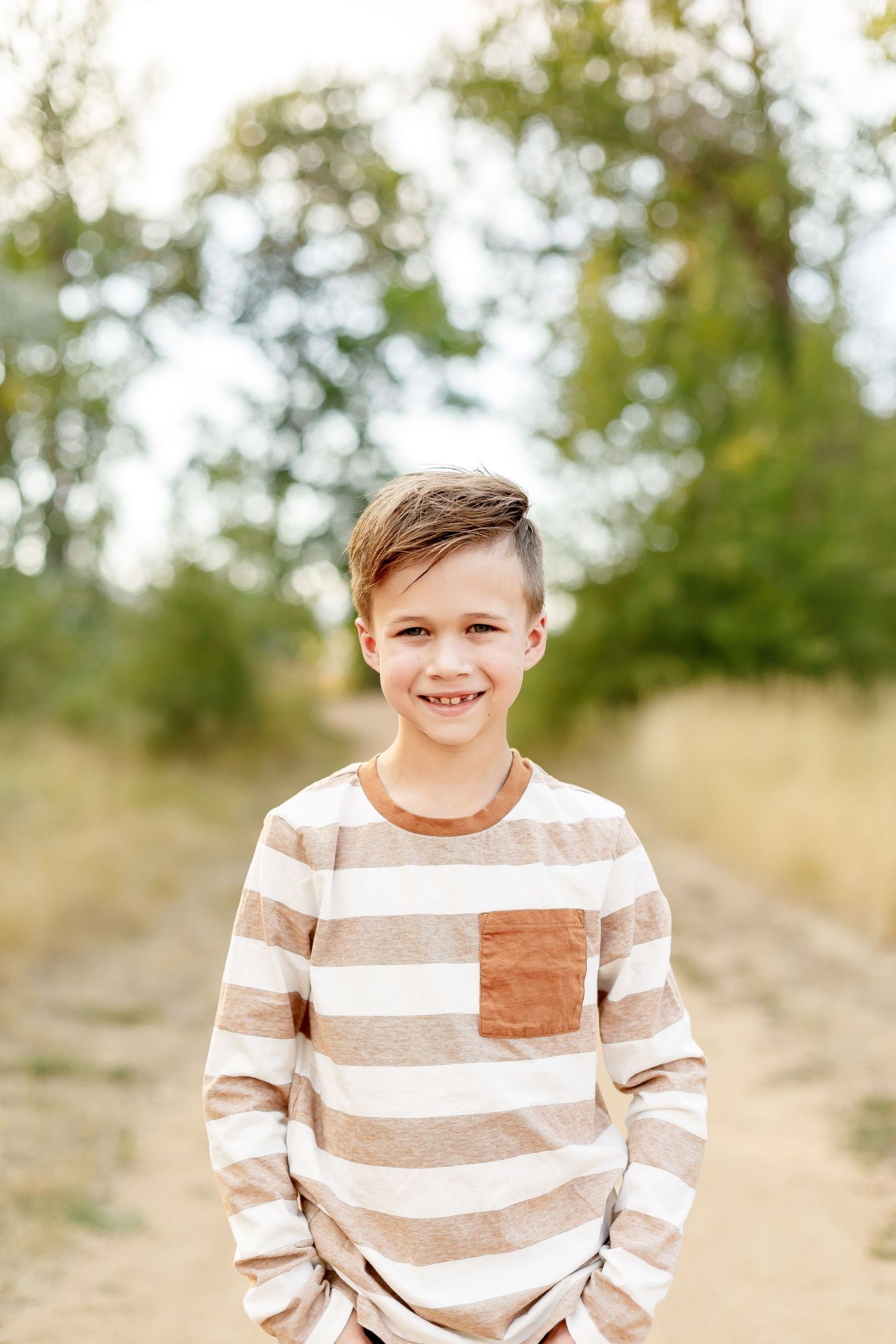 Child wearing brown and white striped sweater smiling outdoors against natural sunny background.