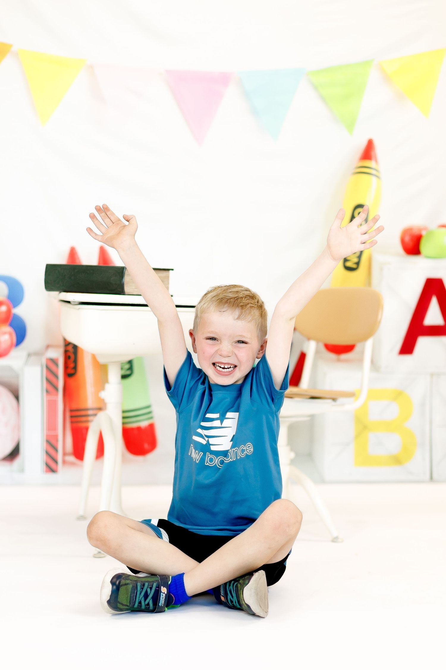 A young child in blue sits on white floor with colorful party decorations and banners in the background.