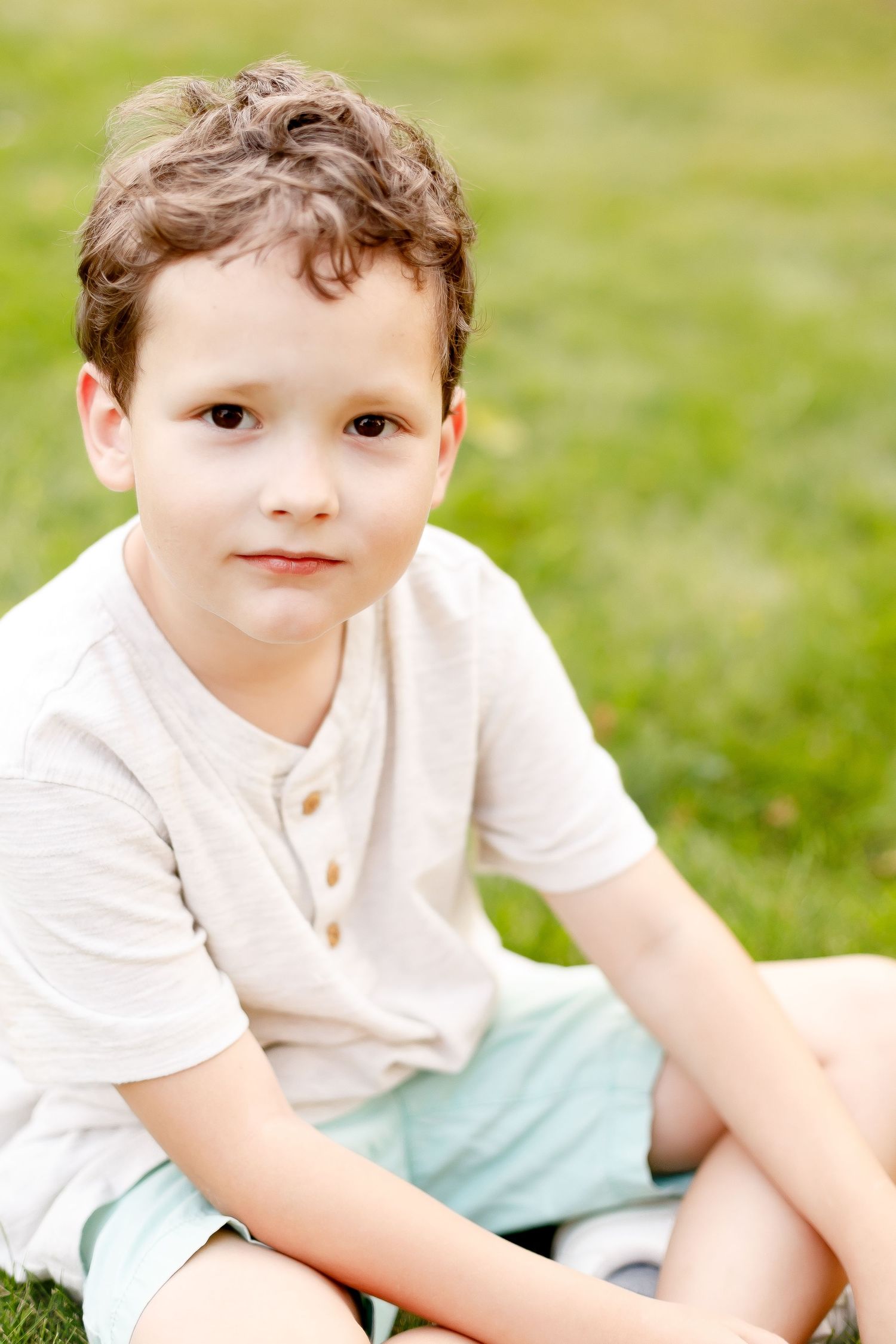 Four sequential photos of a young child sitting outdoors on grass wearing a white shirt and light blue bottoms.