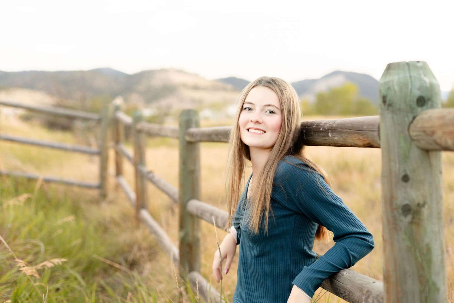 A scenic countryside view with rolling hills and a rustic wooden fence on a sunny afternoon.