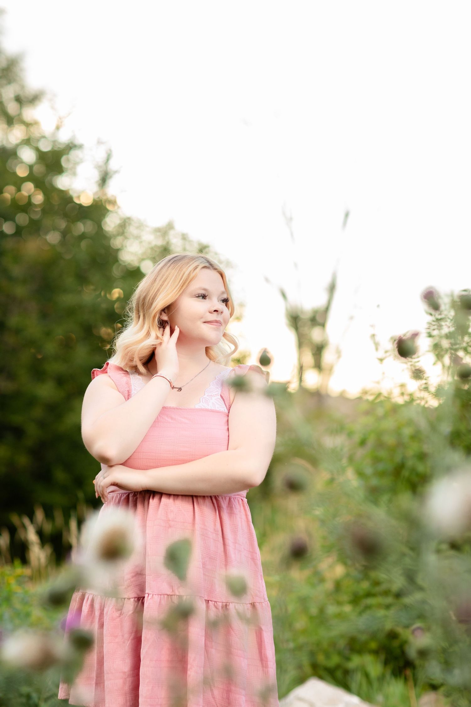 Someone wearing a pink dress poses playfully in a garden setting with soft natural lighting.