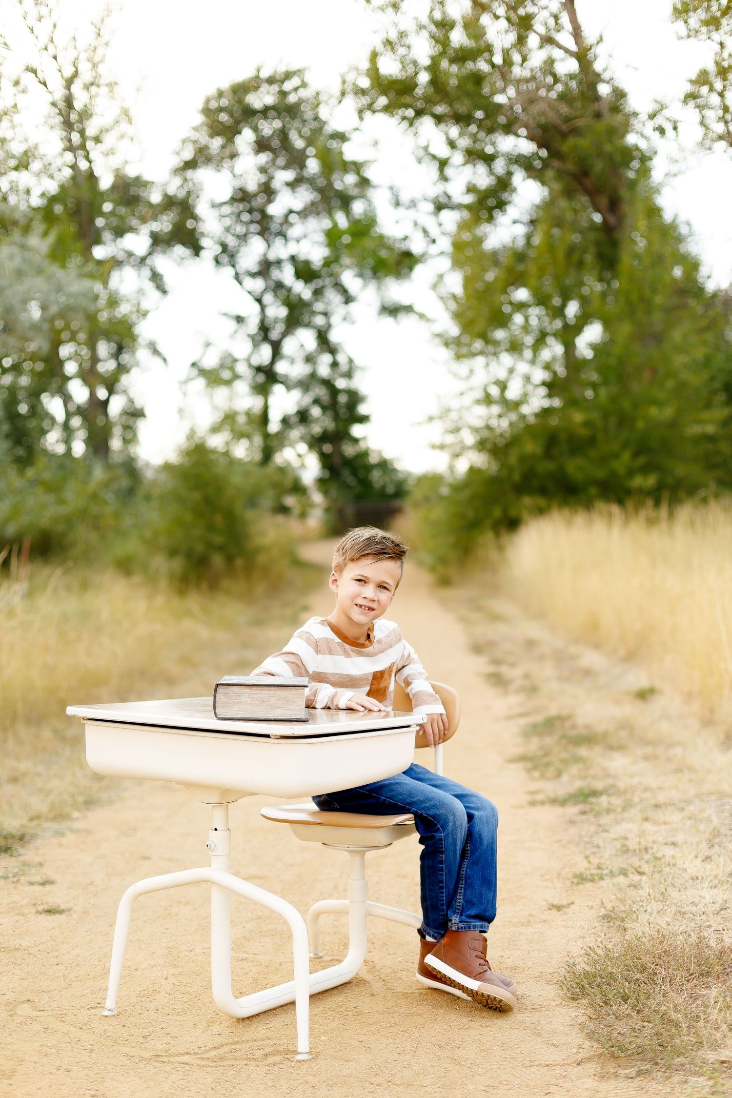 A child in blue jeans lies on a white bench in a natural outdoor setting with tall grass and trees.