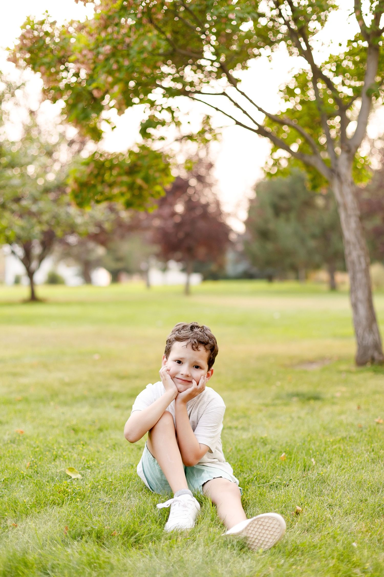 A child sits on the grass in a sunlit park during a golden afternoon.